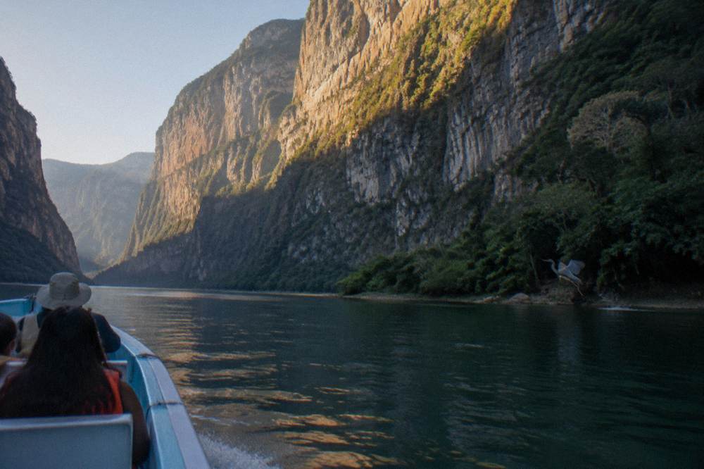 Morning light striking a tall cliff face above still river water