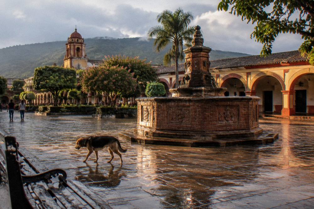 A colonial plaza with a brick fountain and arcades in late afternoon light