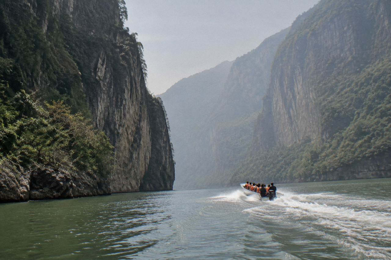Speedboat on a wide river between tall limestone canyon walls under a hazy sky