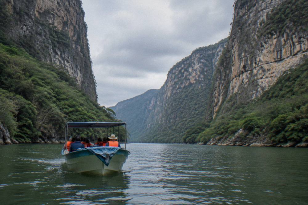 A small motorboat on a wide green river between steep forested canyon walls