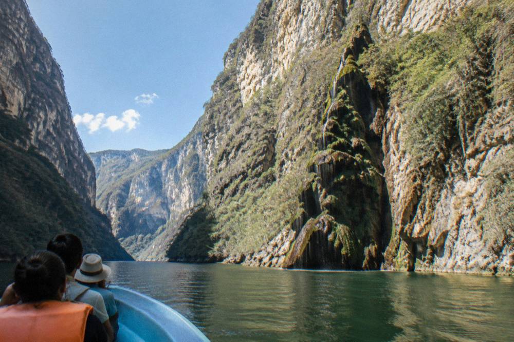 A wide river bend inside the canyon with sunlight striking high rock walls above green water