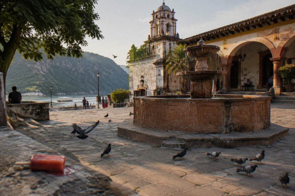 A colonial town square with a brick fountain and arcades under warm afternoon light