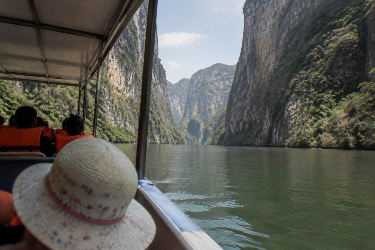 A covered boat cruising calm green water between tall limestone canyon walls