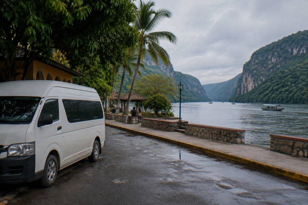 Roadside colectivo van parked beside a tropical street with hills behind