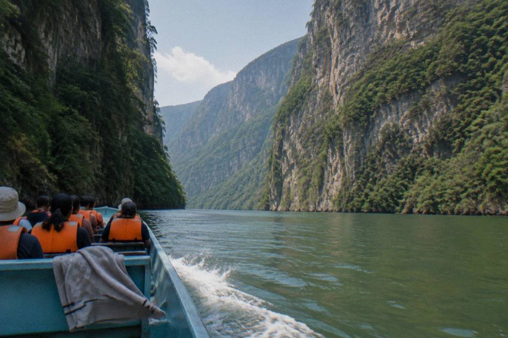 Long wooden boat carrying passengers along a river between steep forested canyon walls