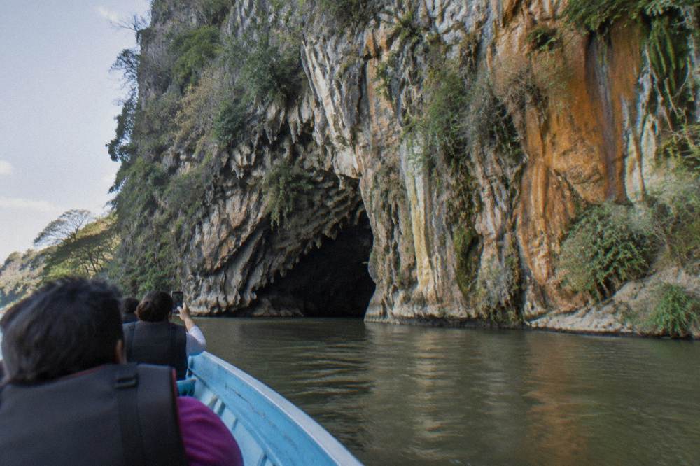 Cave opening in a tall moss covered cliff face above a river