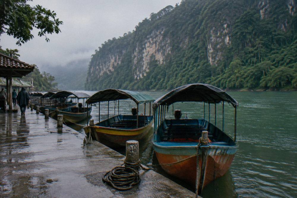Wooden boats moored at a river dock beneath a cliff face