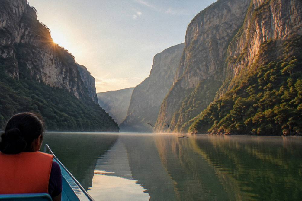 A calm river reflecting tall limestone cliffs in early morning light